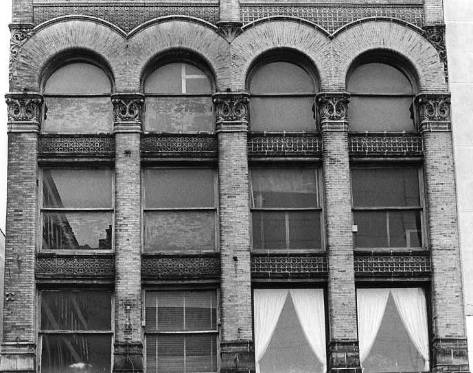 Black and white photo of an old building facade with arched windows and decorative brickwork.