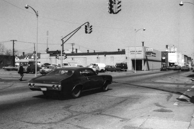 Vintage cars at a traffic light in a black and white photo of an urban street scene.