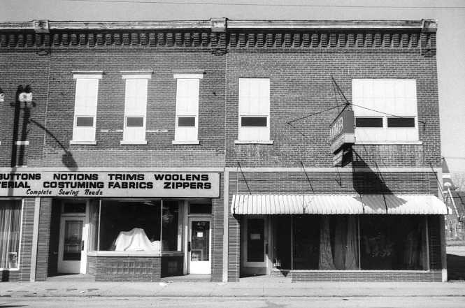 A black and white photo of a two-story brick building with signs for sewing supplies.
