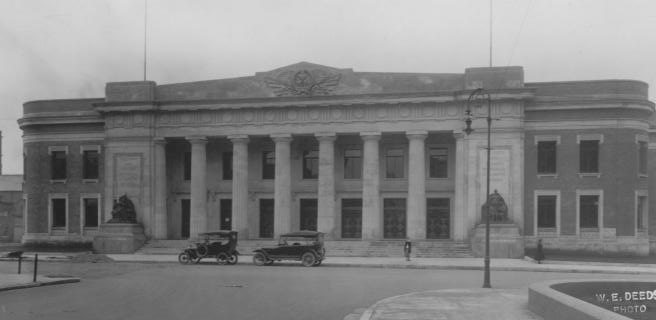 Vintage photo of an old building with columns and classic cars parked outside.