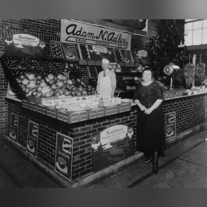 Vintage grocery store with two people amidst fresh produce and product advertisements.