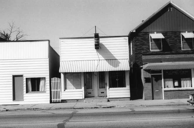 Three adjacent buildings with a mix of residential and commercial styles. Black and white photo.