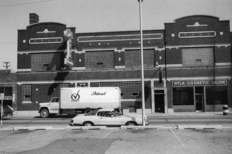 Brick building, "NYLA COSMETIC SALON" sign, parked truck labeled "Ideal," car, and utility pole.