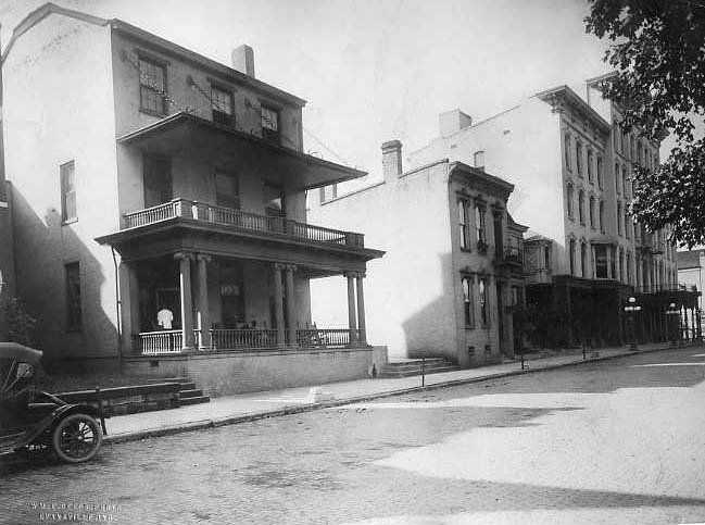 Old photo of a street corner with vintage cars and historic buildings.