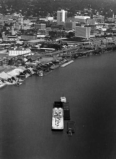 Aerial view of a river with a boat near a city waterfront, showcasing buildings, docks, and urban landscape.