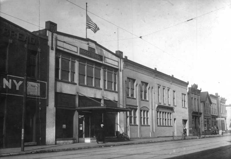 Vintage street scene with old buildings, an American flag, and overhead wires.