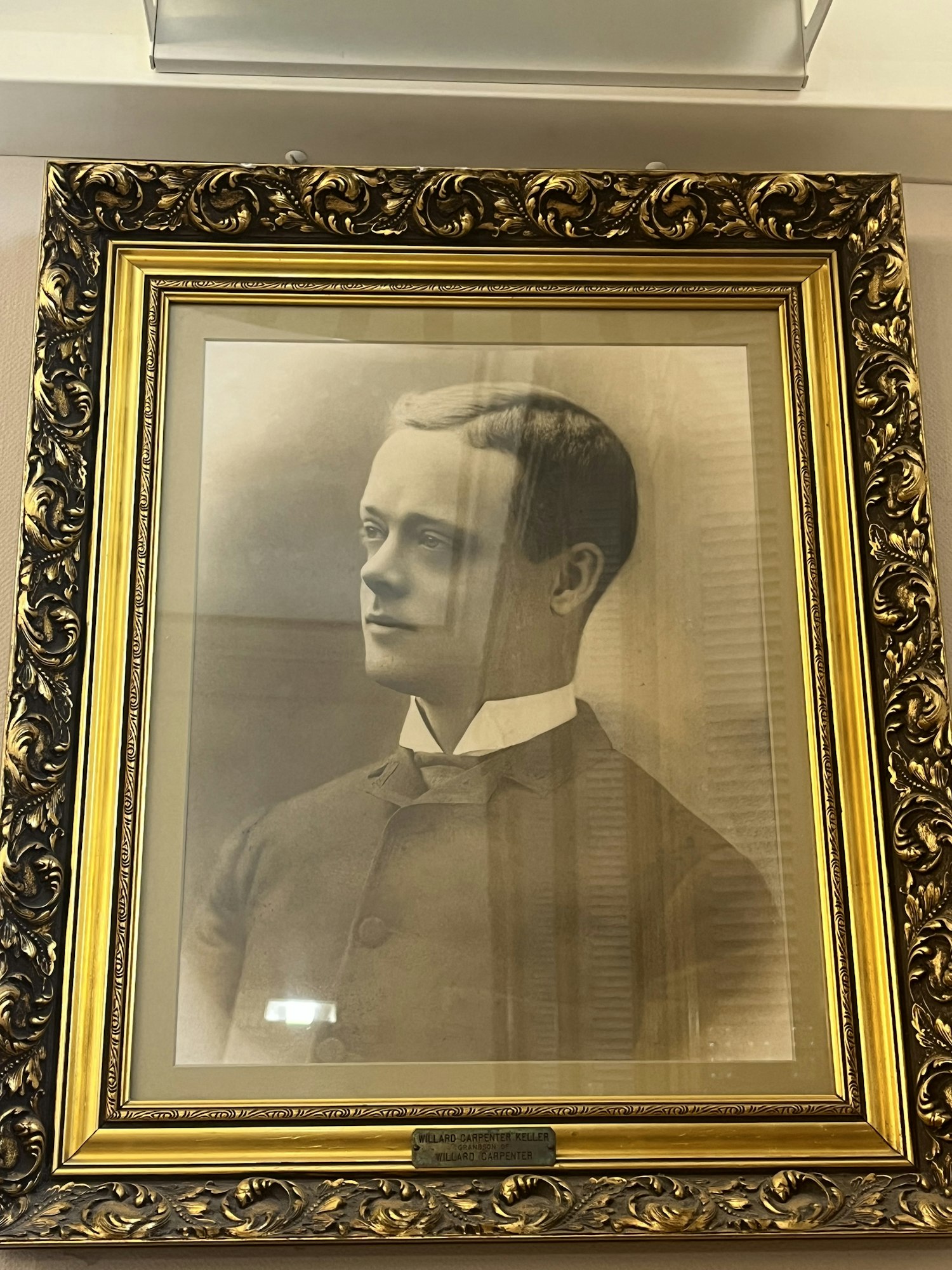 A sepia-toned portrait of a man in a suit with a decorative gold frame, hung on a wall.