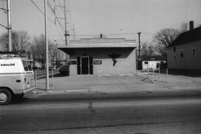 A vintage black-and-white photo of a building with "Coca-Cola" sign, a van marked "Indiana Bell," and utility poles.