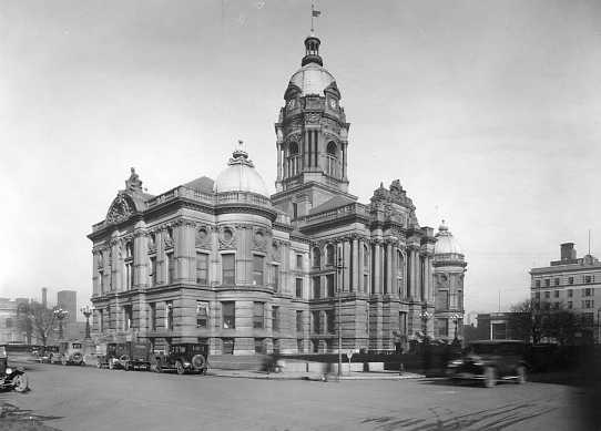 Historic grand building with a dome and vintage cars passing by. Black and white photo.