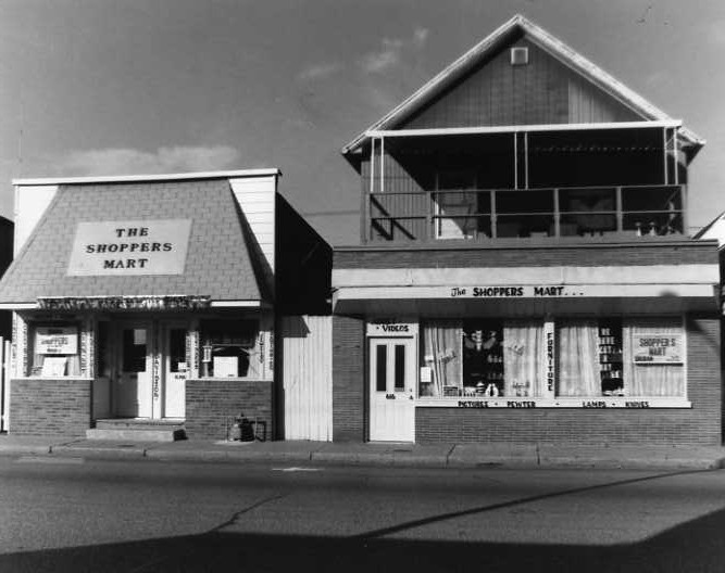 Black and white photo of two adjacent buildings labeled "THE SHOPPERS MART."