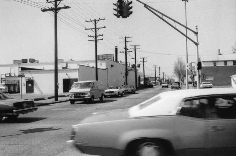 Black and white photo of a street with vintage cars and traffic light.