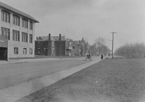 Vintage photo of a street with buildings, a few people, and a telephone pole.