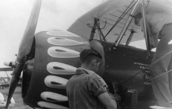 A person is performing maintenance on a vintage airplane with a propeller and large engine cowl vents.