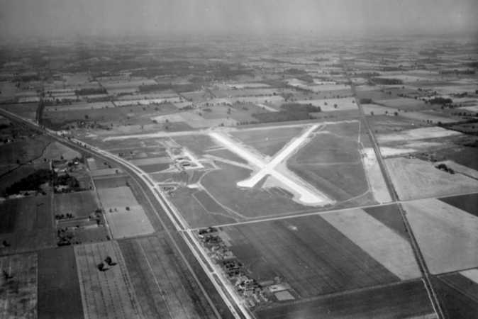 Aerial view of an airfield with intersecting runways, surrounded by open fields.
