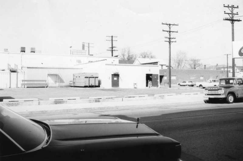 Black and white photo of vehicles and buildings, possibly from the mid-20th century.