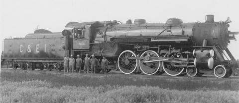 A vintage steam locomotive with a group of people standing in front.