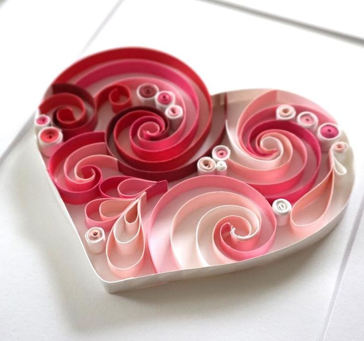 A heart-shaped quilling artwork in shades of pink, featuring intricate swirls and coils.