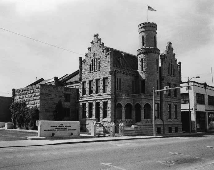 Historic stone building resembling a castle with a turret, American flag flying, clear skies, and street in foreground.