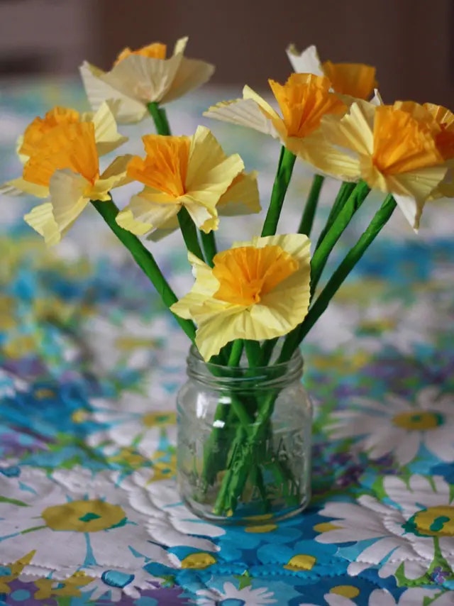 A jar with handmade paper daffodils on a floral tablecloth.