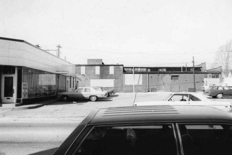 A black and white photo of street with cars and buildings; vintage vibe.