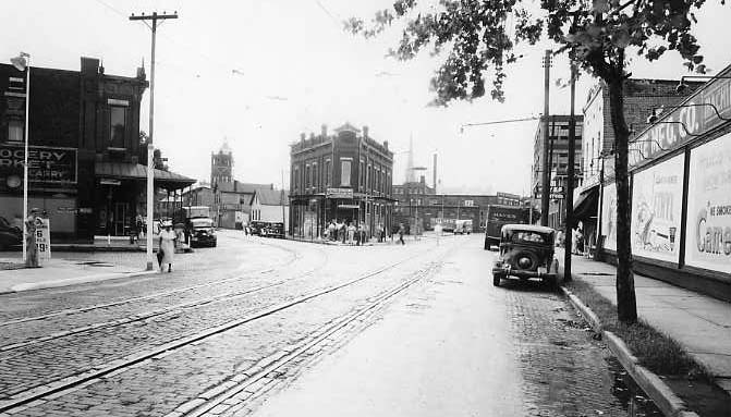 Vintage street scene with tram tracks, old cars, and historic buildings.