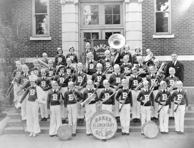 Vintage photo of an elementary school band with instruments, in uniform, posing in front of their school building.