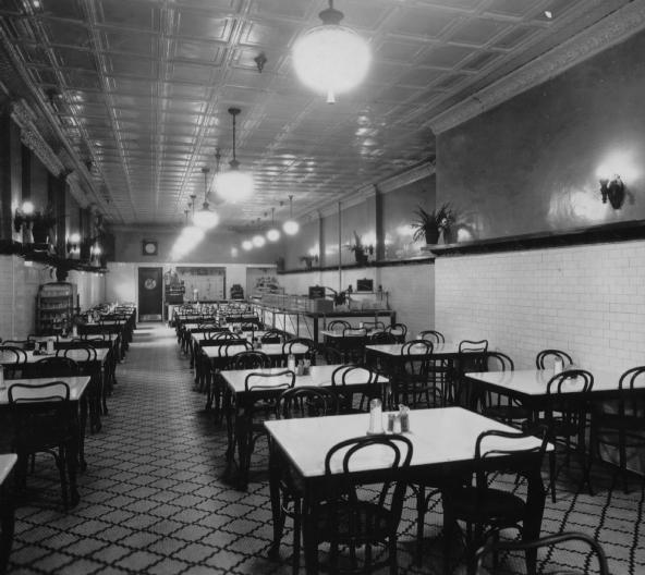 Vintage diner interior with tiled walls, patterned floor, empty tables, and hanging globe lights.
