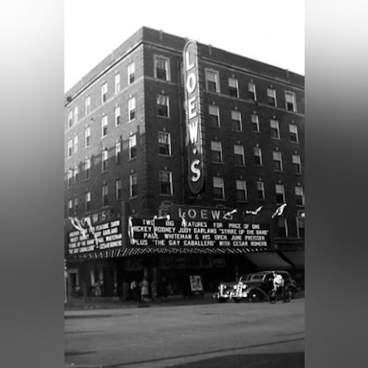 Vintage photo of the Loew's theatre marquee with movies listed and a car parked outside.