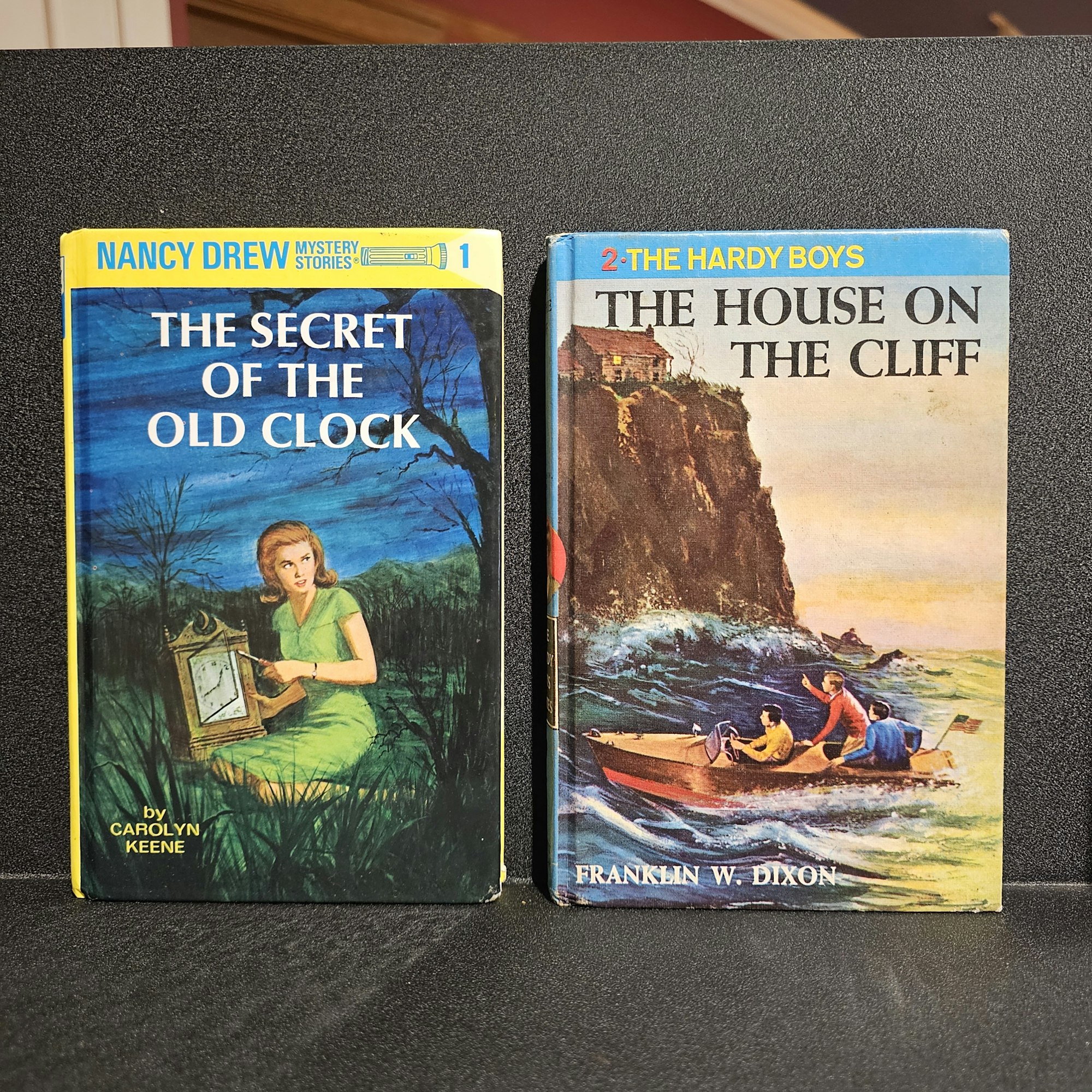Two vintage mystery books: "The Hardy Boys: The House on the Cliff" and "Nancy Drew: The Secret of the Old Clock."