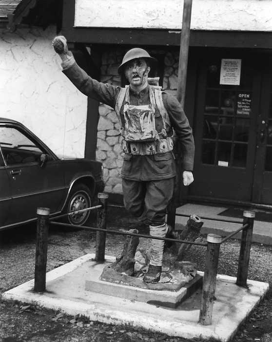 Statue of a miner with raised fist, helmet and gear, next to a car and building. Black and white photo.