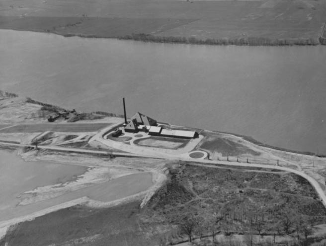 Aerial view of a solitary industrial facility near a large body of water with surrounding land and roads.