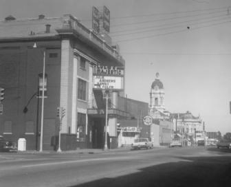 Vintage monochrome photo featuring a street corner, buildings with visible signage, and a tower in the background.