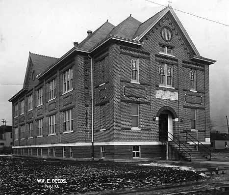 An old black-and-white photo of a two-story brick building with arched entrance and decorative brickwork.