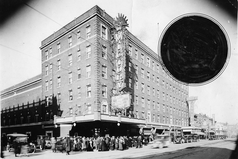 Historic photo of a bustling street scene outside the Victory Theater with a crowd and vintage cars.