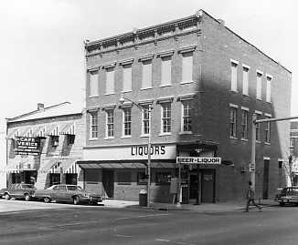 Vintage street corner with liquor store and parked cars in black and white.