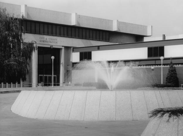 A black and white photo of a city government building with a fountain in front.