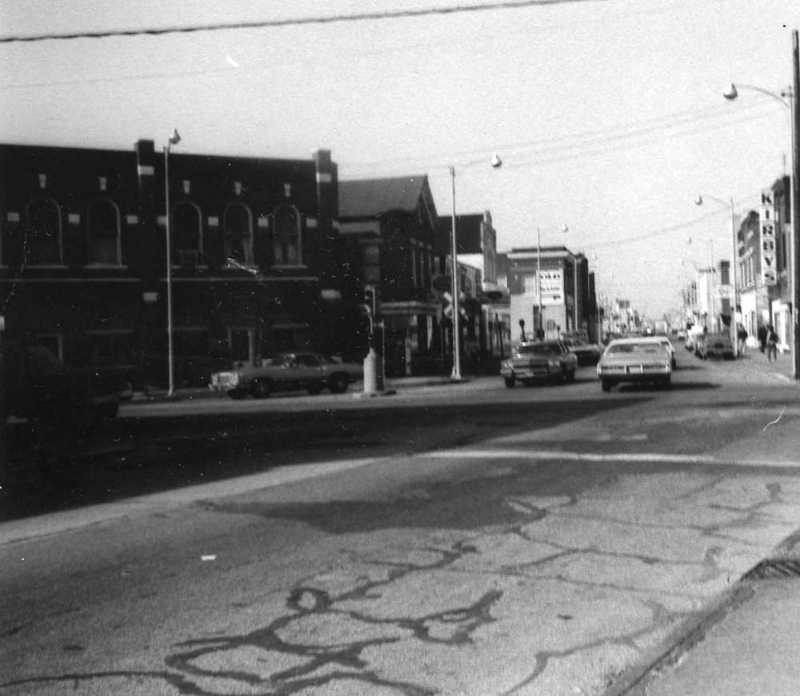 Vintage street view with buildings, cars, and overhead wires.