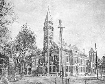 Historic building with a tall tower, intricate architecture, surrounded by trees in a monochrome photo.