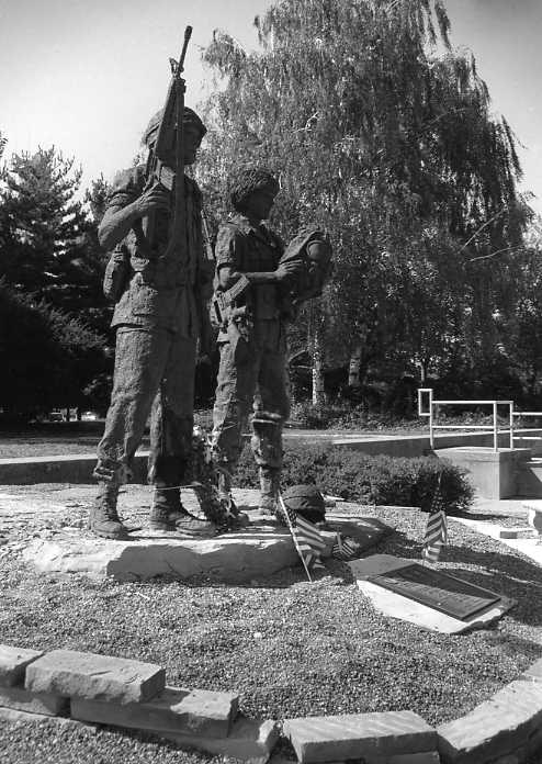 A black and white photo of a military statue with two figures and memorial plaques.