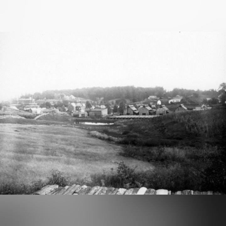Old black and white photo of a rural landscape with houses and sparse vegetation.