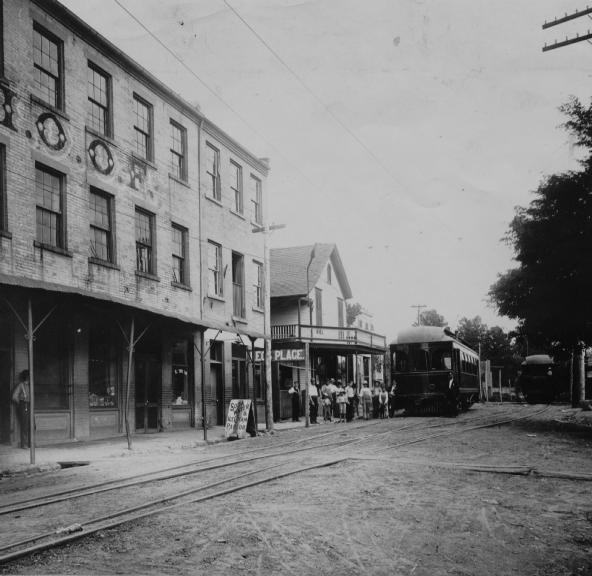 Vintage street view with tram, tracks, buildings, and people.