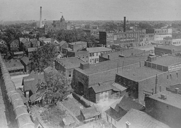 A vintage black and white photo of an industrial townscape with buildings, smokestacks, and old advertisements.