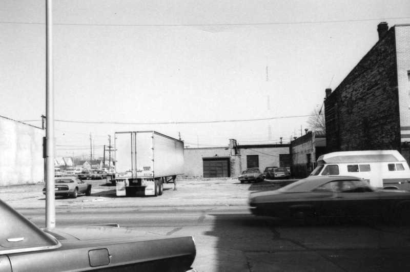 Black and white photo of an urban area with cars, buildings, and a trailer.