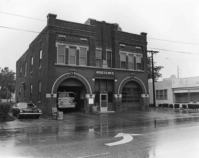 An old fire station, Hose Co. No. 5, with a fire truck and sedan parked, on a rainy day.