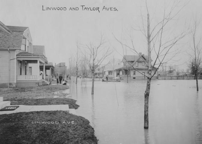 A flooded street with houses and bare trees; signs saying "Linwood and Taylor Aves" and "Linwood Ave."