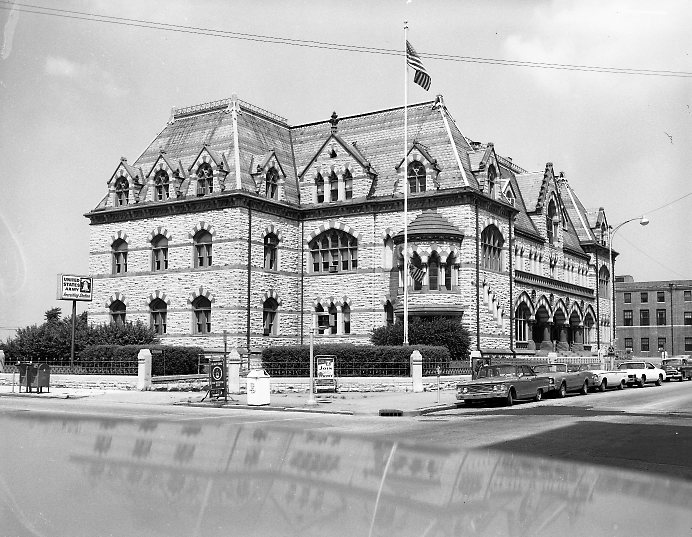 Historic stone building with Gothic features, parked cars, street scene, black and white photo.