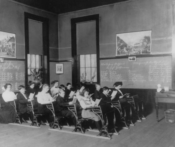Vintage classroom with students and teacher, blackboards cover walls.
