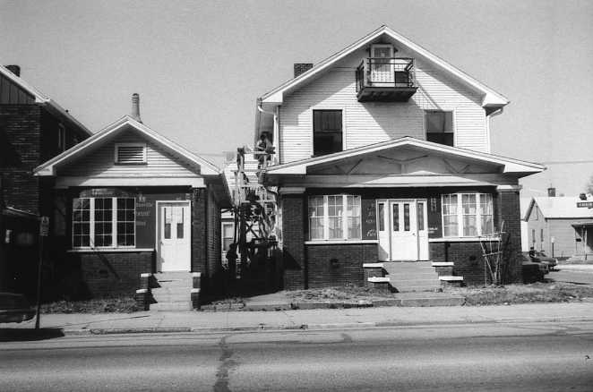Two-story house with a porch, next to a smaller building, in a black and white photo.