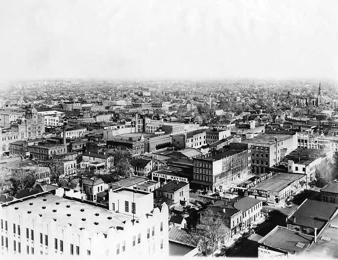 Historic black and white photo of a densely built cityscape with multiple buildings from an aerial perspective.