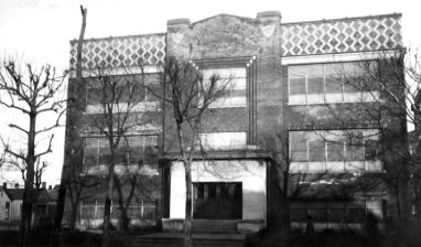 A black and white photo of an old building with decorative patterns on its facade, surrounded by bare trees.